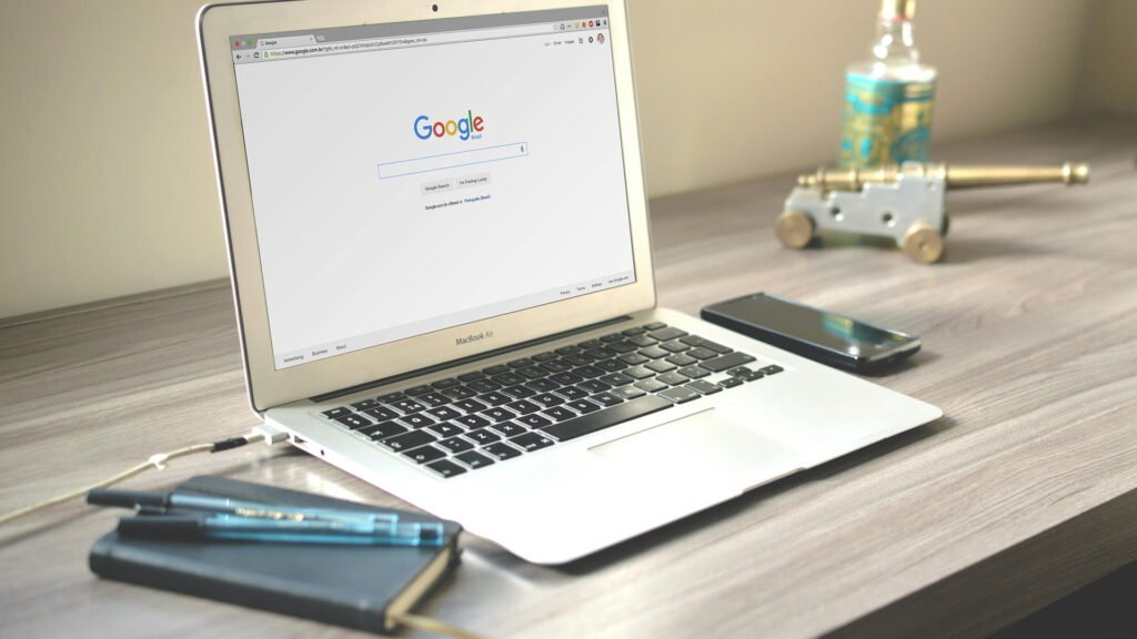 Laptop displaying Google search page on office desk with smartphone and notebook, representing SEO keyword research and digital marketing workspace