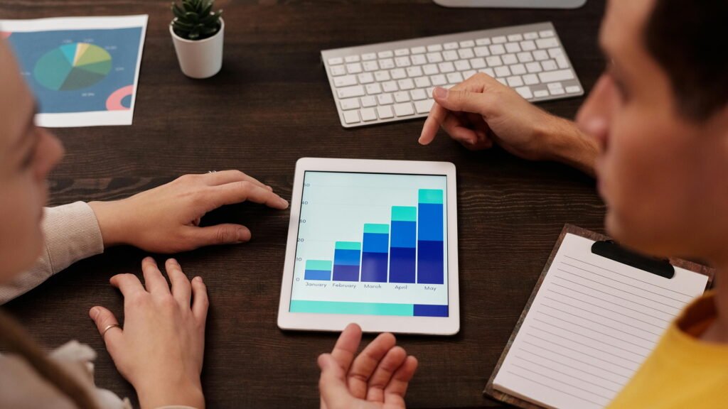 Team at a wooden desk reviewing a tablet bar chart, discussing SEO vs Digital Marketing strategies.
