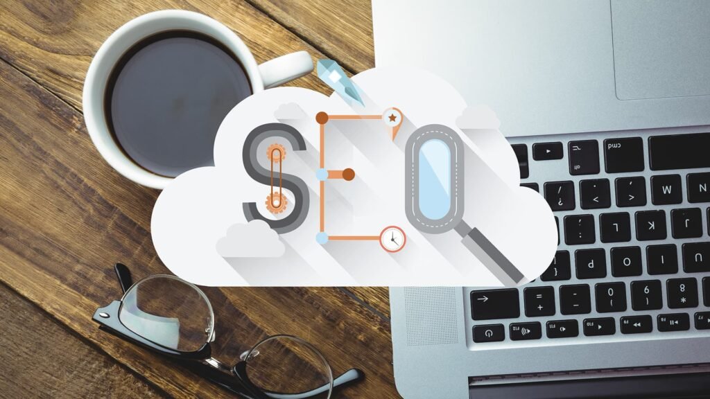 Workspace with coffee, laptop, and eyeglasses featuring SEO cloud graphic with gears and magnifying glass.