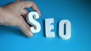 Hand arranging white SEO letters on a blue background, representing SEO optimization tips, search engine ranking, and digital marketing strategy.
