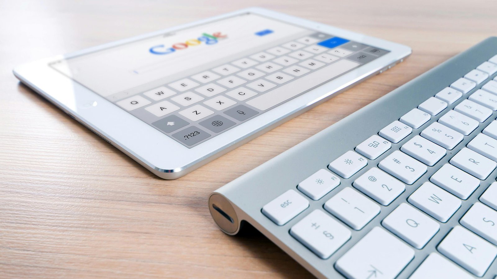 "Sleek tablet on Google search beside a silver wireless keyboard, styled on a light wooden desk — a modern digital workspace blending touch and precision