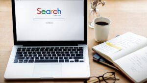 Laptop showing a search engine homepage beside a notebook and coffee cup, representing website ranking, Google search optimization, and SEO research.